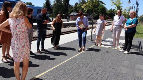 Na zdjęciu grupa osób stojąca przed biblioteką patrzy na kostkę brukową