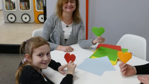 Na zdjęciu bibliotekarka oraz dziewczynka trzymające prace wykonane z origami